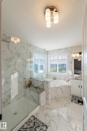 Enclosed shower with glass panel, built-in bench with stone top, and large format wall and floor tiling - 914 Crystallina Nera Way Nw, Edmonton, AB 