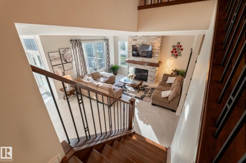 Living area featuring a stone-clad fireplace with a wood mantel, tile flooring, and large windows - 914 Crystallina Nera Way Nw, Edmonton, AB 