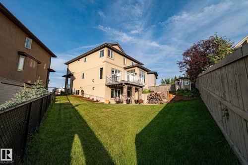 Expansive backyard with a manicured lawn, a multi-level deck featuring glass railings, and a lower patio area with stone-clad columns - 914 Crystallina Nera Way Nw, Edmonton, AB 