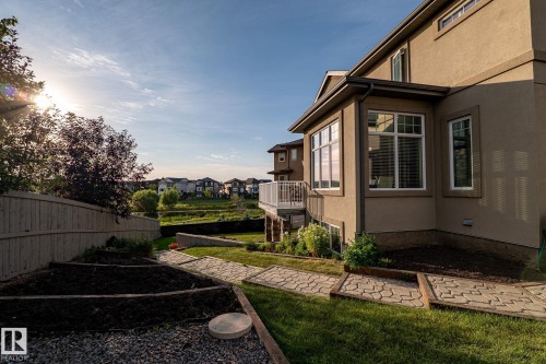Exterior featuring stucco siding, multiple windows with white trim, a balcony with white railings, a landscaped yard with a pathway, and terraced garden beds - 914 Crystallina Nera Way Nw, Edmonton, AB 
