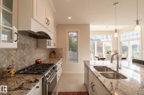 White cabinetry, stainless steel appliances, patterned backsplash, granite countertops, and a double basin sink - 914 Crystallina Nera Way Nw, Edmonton, AB 