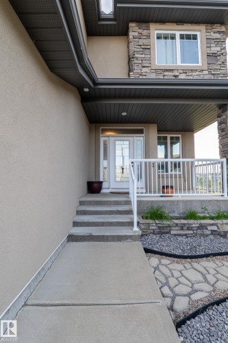 Stucco and stone facade with a covered entry, concrete walkway, and patterned paver accent - 914 Crystallina Nera Way Nw, Edmonton, AB 
