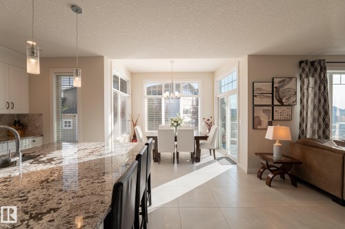 Open concept living space featuring a kitchen island with granite countertop, built-in cabinetry, and pendant lighting - 914 Crystallina Nera Way Nw, Edmonton, AB 