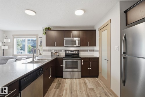 Kitchen featuring dark wood cabinetry, stainless steel appliances, a double basin sink, and wood-finish flooring - 17621 10 Avenue Sw, Edmonton, AB - Indoor Photo Showing Kitchen With Double Sink With Upgraded Kitchen