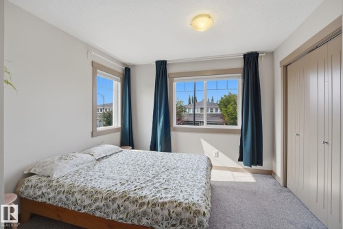 Carpeted bedroom featuring multiple windows with wood-finish trim, a flush-mount ceiling light, and a built-in closet with vertical panel doors - 17621 10 Avenue Sw, Edmonton, AB - Indoor Photo Showing Bedroom