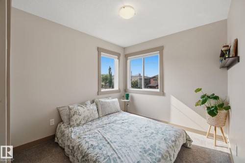 Bedroom featuring light-toned walls, two windows with wood-trim framing, a flush-mount ceiling light fixture, and textured carpeting - 17621 10 Avenue Sw, Edmonton, AB - Indoor Photo Showing Bedroom