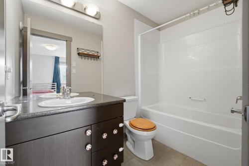 Master bathroom featuring a single vanity with a dark wood-finish cabinet and stone-look countertop, a white sink with a chrome faucet, and a combination tub and shower with white surround panels - 17621 10 Avenue Sw, Edmonton, AB - Indoor Photo Showing Bathroom