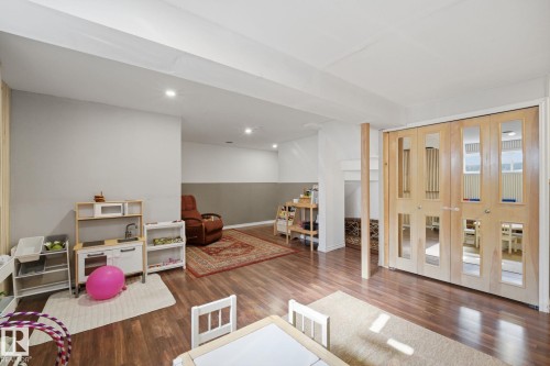 Spacious finished lower level featuring wood-finish flooring, recessed lighting, a two-tone wall treatment, and light wood bi-fold doors hiding the laundry - 17621 10 Avenue Sw, Edmonton, AB - Indoor