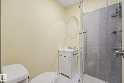 Full bathroom featuring a glass-enclosed shower with gray subway tile surround, white vanity with integrated sink, and a circular wall mirror - 17621 10 Avenue Sw, Edmonton, AB - Indoor Photo Showing Bathroom