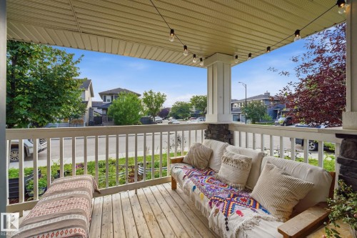 Covered porch featuring natural wood decking, stone-clad pillars, and a white railing - 17621 10 Avenue Sw, Edmonton, AB - Outdoor With Deck Patio Veranda With Exterior