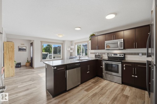Kitchen featuring wood-finish flooring, dark wood cabinetry, stainless steel appliances, and a tiled backsplash - 17621 10 Avenue Sw, Edmonton, AB - Indoor Photo Showing Kitchen