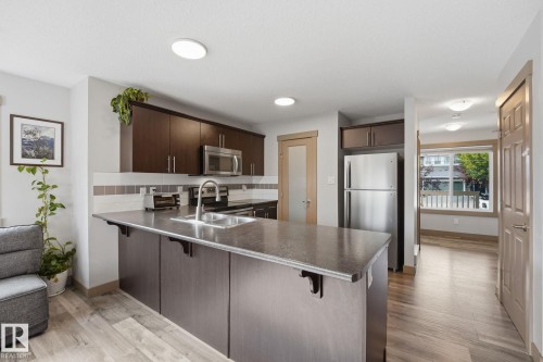 Kitchen featuring dark wood-finish cabinetry, stainless steel appliances, and wood-finish flooring - 17621 10 Avenue Sw, Edmonton, AB - Indoor Photo Showing Kitchen With Double Sink