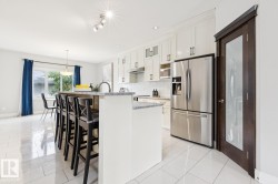 Expansive kitchen island with seating, stainless steel appliances, white cabinetry with display features, tiled flooring, and a glass-paneled interior door - 