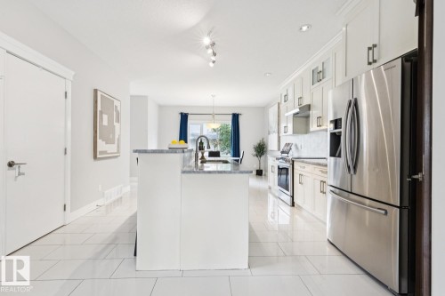 Contemporary kitchen featuring stainless steel appliances, white cabinetry, a center island with a sink, and light-toned tile flooring - 9919 79 Street Nw, Edmonton, AB 