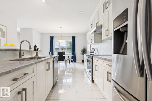 Sleek kitchen featuring white cabinetry, stone countertops, stainless steel appliances, and tile flooring - 9919 79 Street Nw, Edmonton, AB 