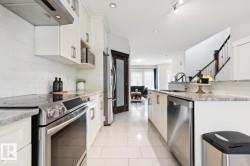 White cabinetry with stainless steel appliances, light-toned tile flooring, and granite countertops - 