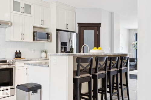 White shaker cabinetry, stainless steel appliances, subway tile backsplash, and a multi-level island with seating - 9919 79 Street Nw, Edmonton, AB 