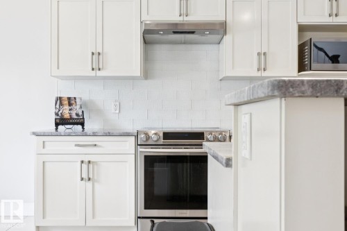 White shaker-style cabinetry with brushed nickel hardware, sleek stainless steel range, coordinating stainless steel range hood, and white subway tile backsplash - 9919 79 Street Nw, Edmonton, AB 