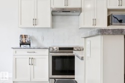 White shaker-style cabinetry with brushed nickel hardware, sleek stainless steel range, coordinating stainless steel range hood, and white subway tile backsplash - 