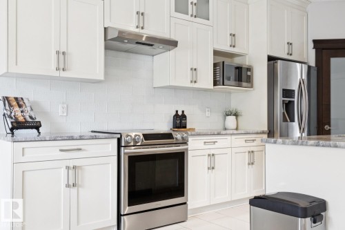 White shaker-style cabinetry with brushed nickel hardware, stainless steel appliances, textured white subway tile backsplash, and light-toned countertops - 9919 79 Street Nw, Edmonton, AB 