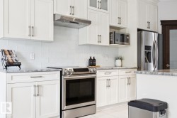 White shaker-style cabinetry with brushed nickel hardware, stainless steel appliances, textured white subway tile backsplash, and light-toned countertops - 