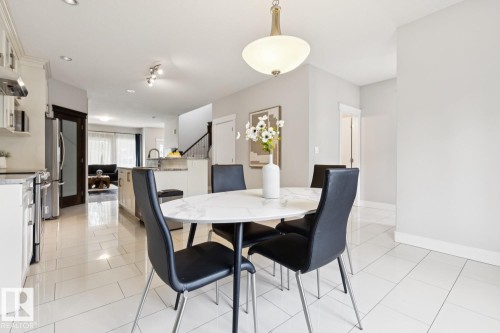 White tile flooring, white shaker cabinetry, stainless steel appliances, a kitchen island with seating, and a modern pendant light fixture - 9919 79 Street Nw, Edmonton, AB 