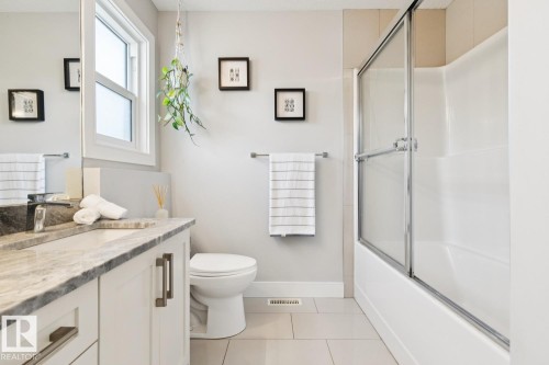 Modern bathroom featuring a single-pane window, a vanity with a stone countertop, an undermount sink, and a shower-tub combination with a glass enclosure - 9919 79 Street Nw, Edmonton, AB 