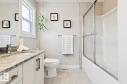 Modern bathroom featuring a single-pane window, a vanity with a stone countertop, an undermount sink, and a shower-tub combination with a glass enclosure - 