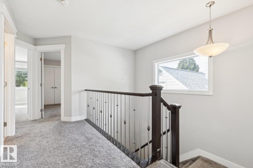 Staircase featuring dark wood handrail, metal balusters, and a contemporary pendant light fixture - 9919 79 Street Nw, Edmonton, AB 