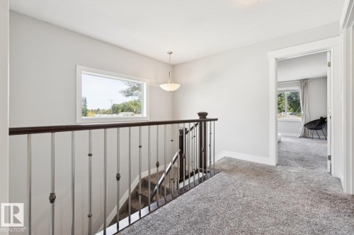 Carpeted hallway with a staircase featuring dark wood newel posts and railings, white balusters, and a rectangular window - 9919 79 Street Nw, Edmonton, AB 