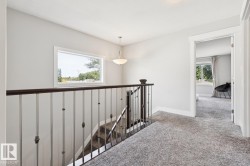 Carpeted hallway with a staircase featuring dark wood newel posts and railings, white balusters, and a rectangular window - 