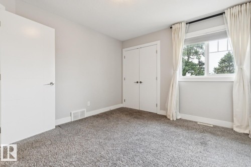 Spacious bedroom with neutral wall finishes, plush carpeting throughout, and abundant natural light from a large dual-pane window with custom drapery - 9919 79 Street Nw, Edmonton, AB 