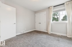 Spacious bedroom with neutral wall finishes, plush carpeting throughout, and abundant natural light from a large dual-pane window with custom drapery - 
