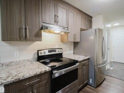 Wood-finish cabinetry with silver-tone hardware, granite countertops, stainless steel appliances, white subway tile backsplash, and wood-finish flooring - 