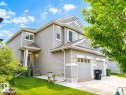 Two-story exterior with light gray siding, prominent gable dormers, attached garage with sectional doors, concrete driveway, and front lawn - 5407 14 Avenue Sw, Edmonton, AB 