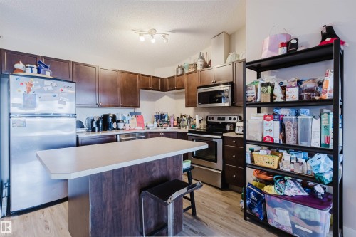 Kitchen featuring stainless steel appliances, wood-finish cabinetry, a central island with a light-toned countertop, and wood-finish flooring - #7428 7327 South Terwillegar Dr Nw, Edmonton, AB 