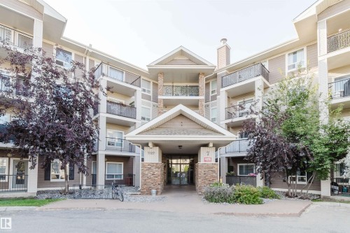 Multi-story building featuring stacked balconies with black metal railings, a central stone-clad entrance, and a gabled portico - #7428 7327 South Terwillegar Dr Nw, Edmonton, AB 