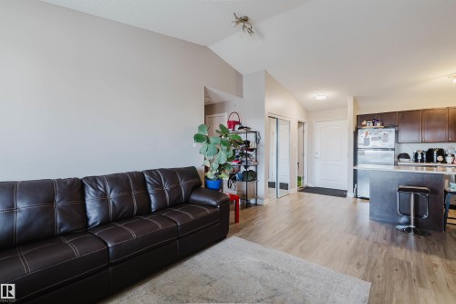 Open-concept living space featuring wood-finish flooring, a kitchen island with seating, dark wood cabinetry, and stainless steel appliances - #7428 7327 South Terwillegar Dr Nw, Edmonton, AB 