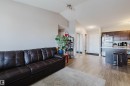 Open-concept living space featuring wood-finish flooring, a kitchen island with seating, dark wood cabinetry, and stainless steel appliances - #7428 7327 South Terwillegar Dr Nw, Edmonton, AB 