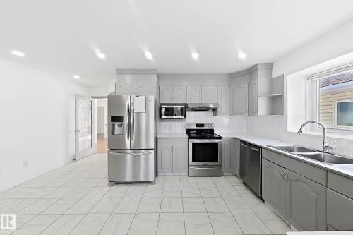 Kitchen featuring stainless steel appliances, light gray cabinetry, white tile flooring, white countertops, and a double basin sink - 3015 37 Street Nw, Edmonton, AB 