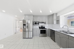 Kitchen featuring stainless steel appliances, light gray cabinetry, white tile flooring, white countertops, and a double basin sink - 