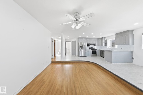 Wood-finish flooring with a curved transition to tiled flooring, a kitchen featuring light gray cabinetry, stainless steel appliances, and recessed lighting - 3015 37 Street Nw, Edmonton, AB 