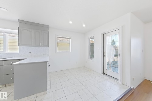 Bright, open kitchen and dining area featuring gray cabinetry with ample storage, white subway tile backsplash, tile flooring, recessed lighting, and glass sliding door access to the exterior - 3015 37 Street Nw, Edmonton, AB 