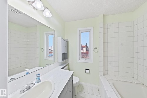 Bright bathroom featuring a large vanity with dual sink setup, white subway tile walls, frameless glass shower enclosure, and abundant natural light from multiple windows overlooking the cityscape - 3015 37 Street Nw, Edmonton, AB 