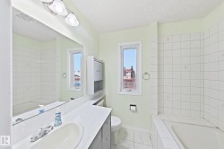 Bright bathroom featuring a large vanity with dual sink setup, white subway tile walls, frameless glass shower enclosure, and abundant natural light from multiple windows overlooking the cityscape - 