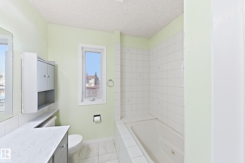 Bathroom featuring a built-in bathtub, white wall tiling, and a window with natural light - 3015 37 Street Nw, Edmonton, AB 