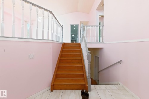 Hardwood staircase with painted balusters, white tile flooring, and vaulted ceiling - 3015 37 Street Nw, Edmonton, AB 