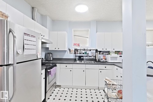 Kitchen featuring white cabinetry, dark countertops, stainless steel appliances, and patterned floor tiling - 3015 37 Street Nw, Edmonton, AB 