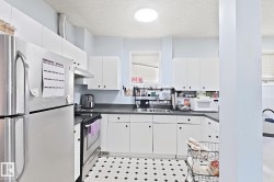 Kitchen featuring white cabinetry, dark countertops, stainless steel appliances, and patterned floor tiling - 