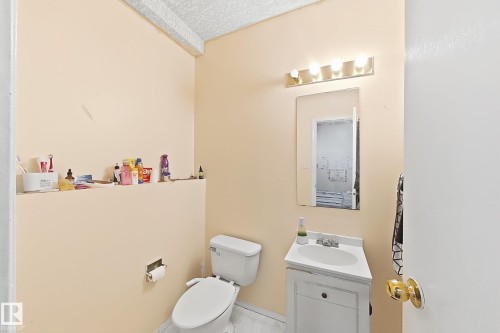 Compact half bath featuring a white porcelain toilet, pedestal sink with chrome faucet, and mirrored medicine cabinet with integrated vanity lighting - 3015 37 Street Nw, Edmonton, AB 